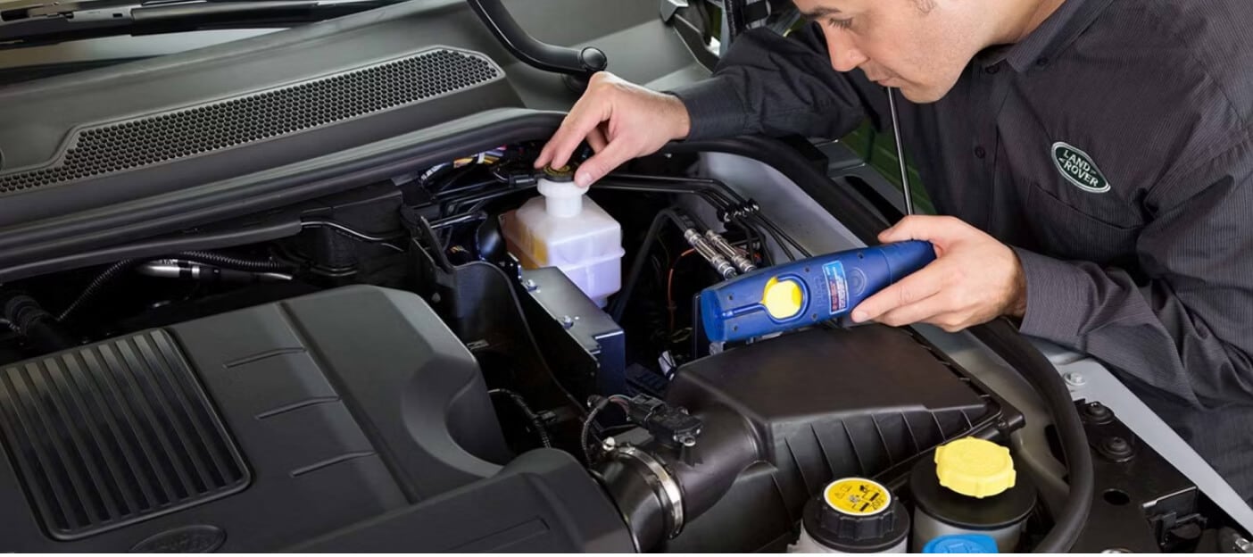 Close-up view of a Range Rover engine being inspected by a technician holding a light in a service bay.