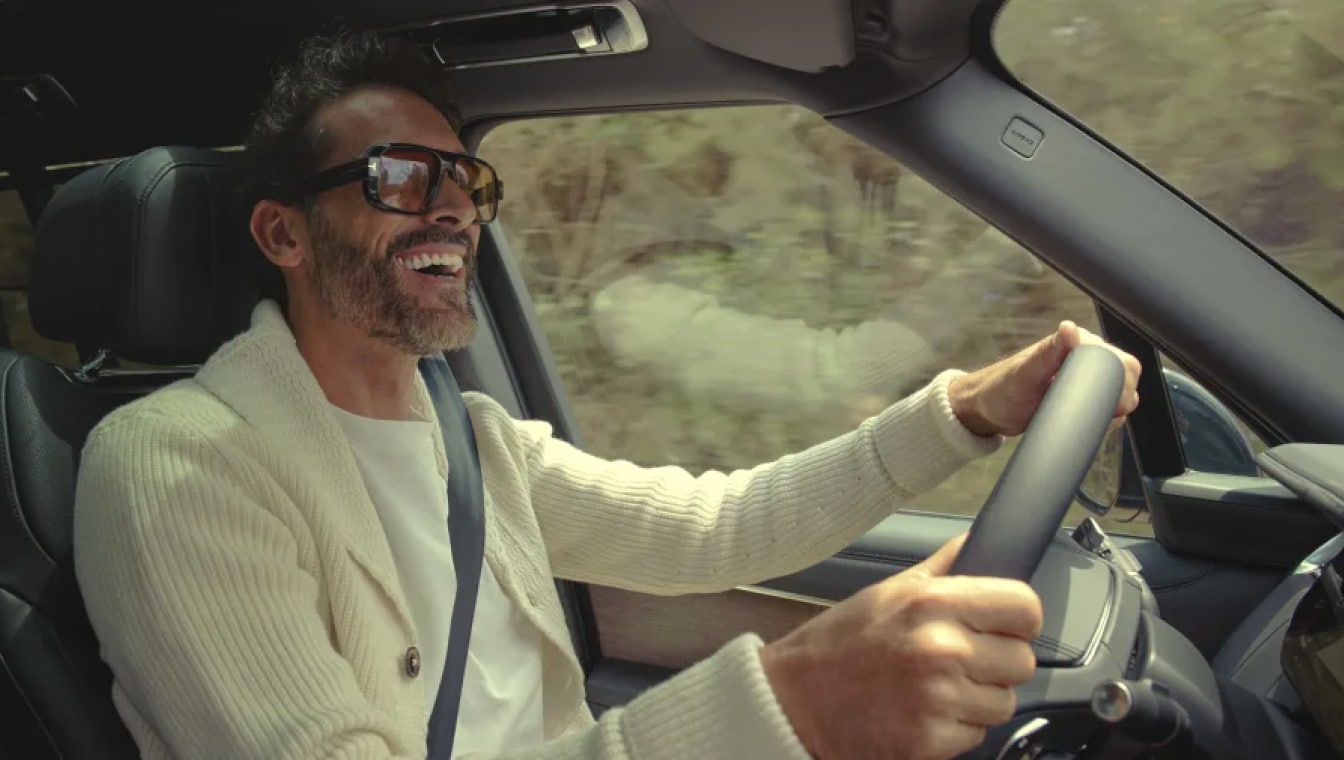 Interior shot of a Range Rover. A man smiles while driving down a stone alleyway.