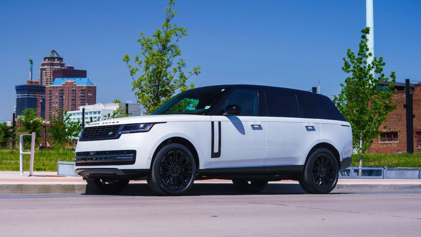 Exterior side view of a white Range Rover parked in front of a Des Moines skyline background.
