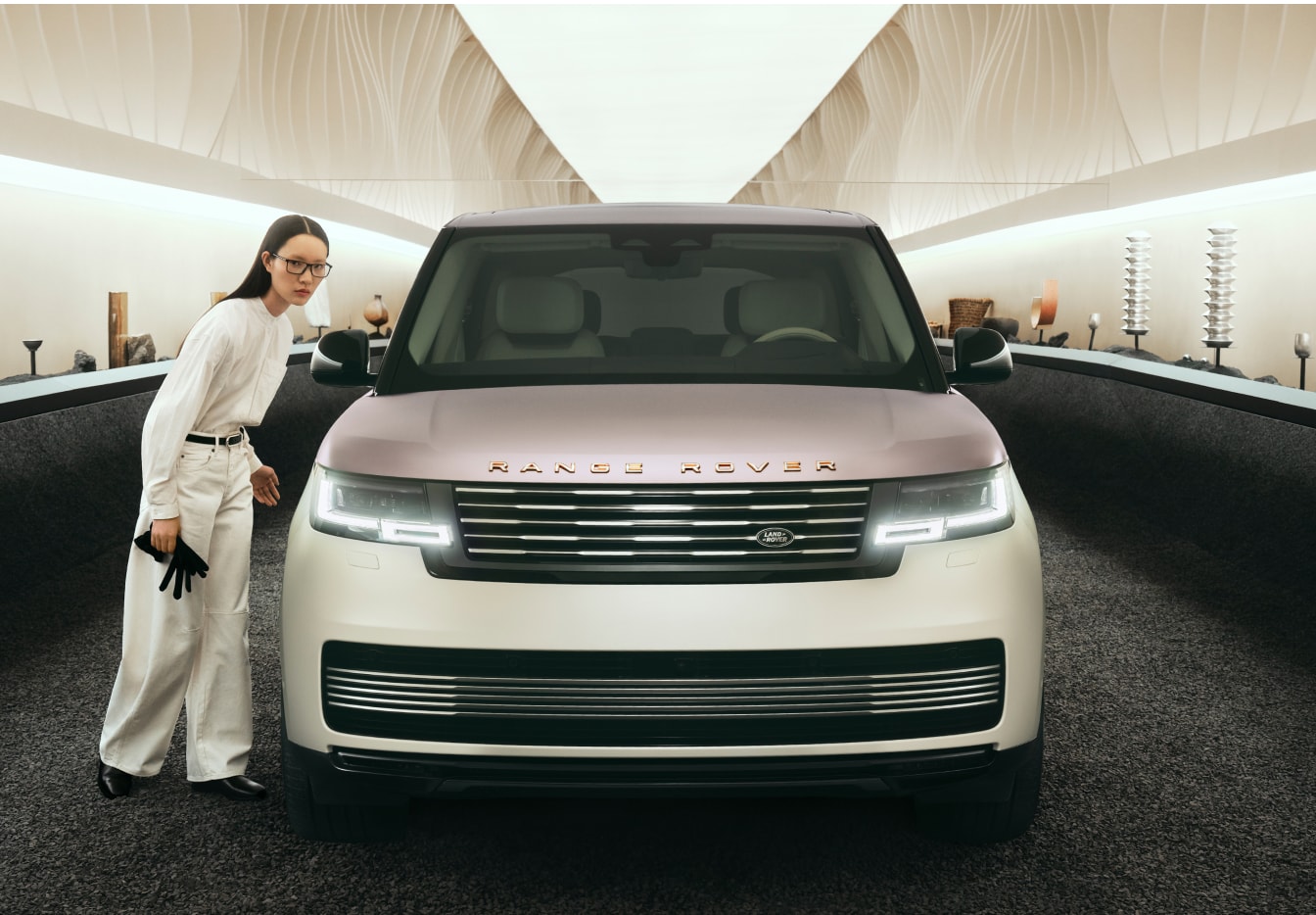 Front exterior view of a Range Rover inside an art gallery. A woman stands nearby admiring it.