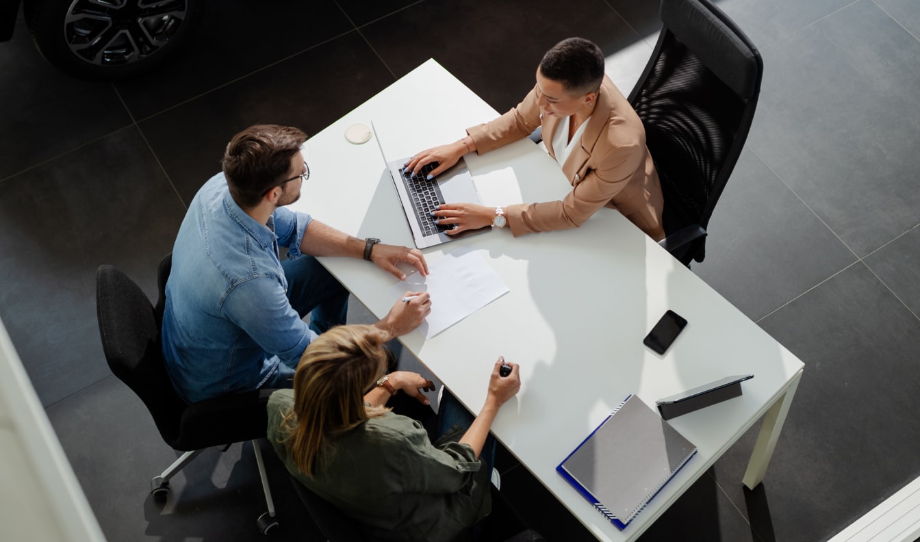 Top down view of a dealership associate assisting a couple navigate financing at a desk.