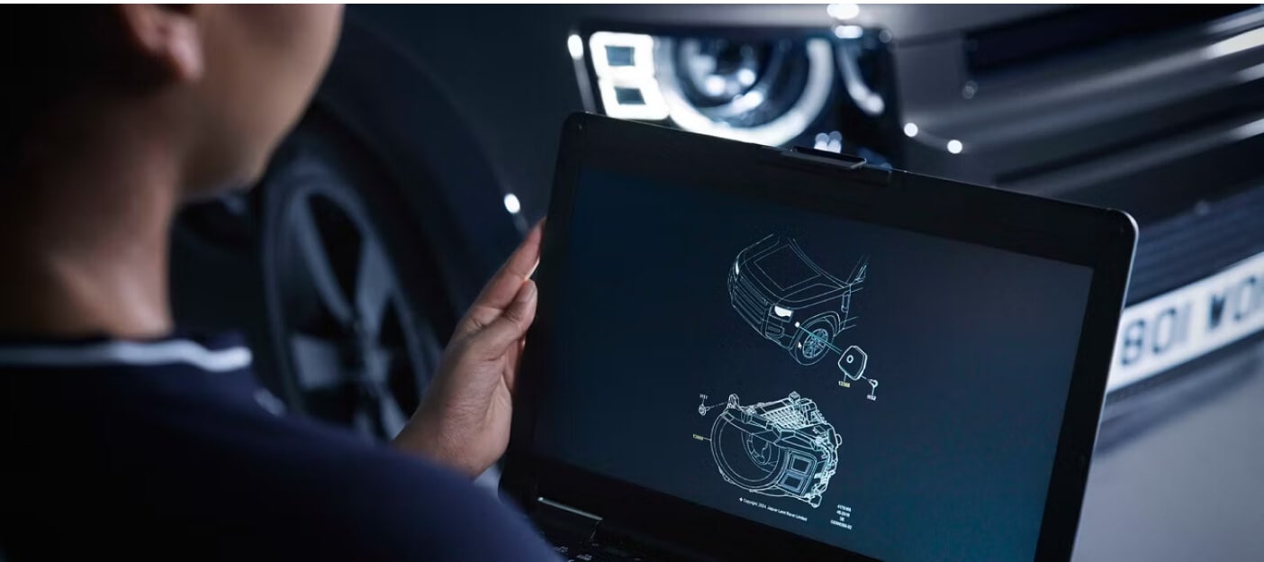 Over-the-shoulder view of a Defender with technician reviewing schematics on a laptop.