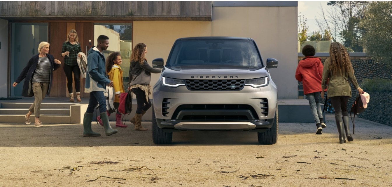 Exterior front view of a family entering silver Discovery in their driveway.