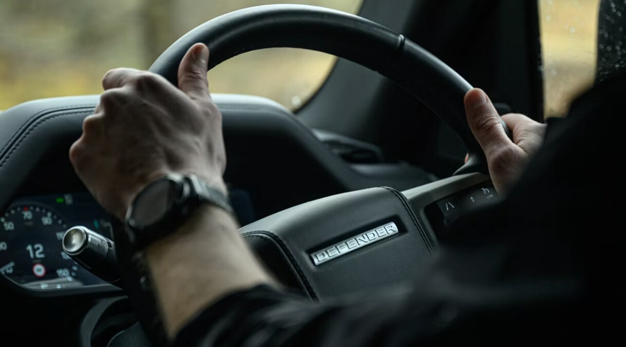 Close-up view of a driver with two hands on a Defender SUV steering wheel