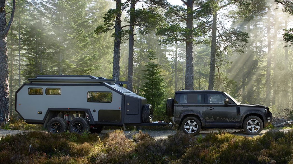 Side profile view of the 2025 Defender 90 towing a trailer through a forest