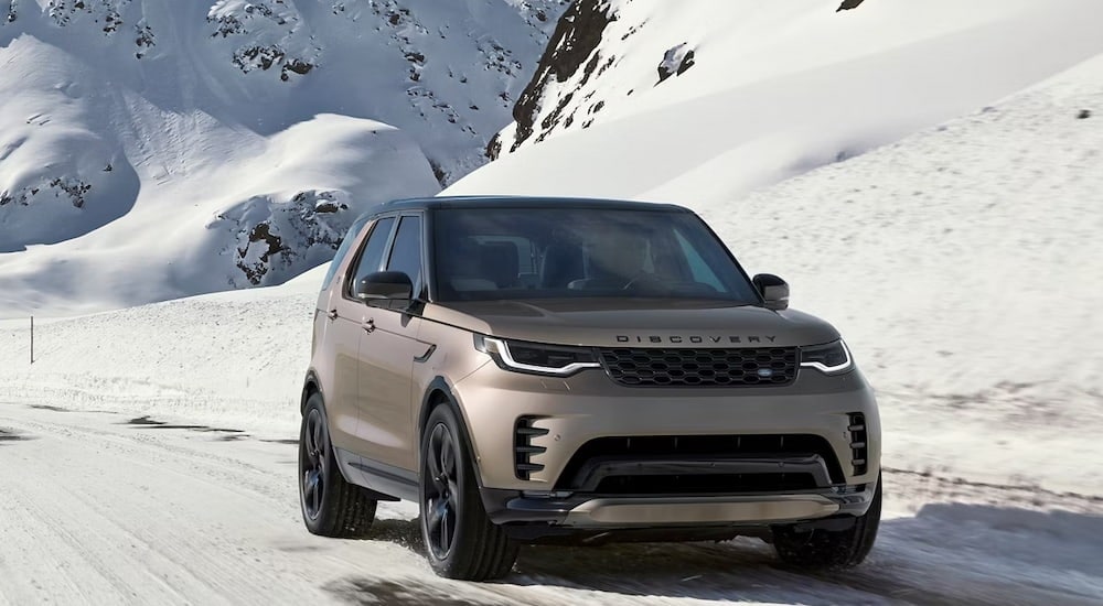 Tan 2026 Land Rover Discovery driving on a snowy road.