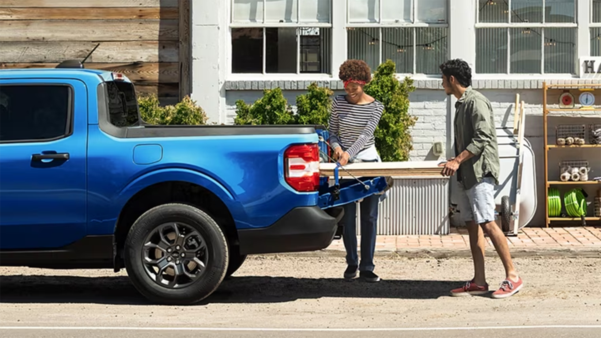 A red Ford Maverick® pickup with gardening items and lumber in the bed, with the tailgate lowered
