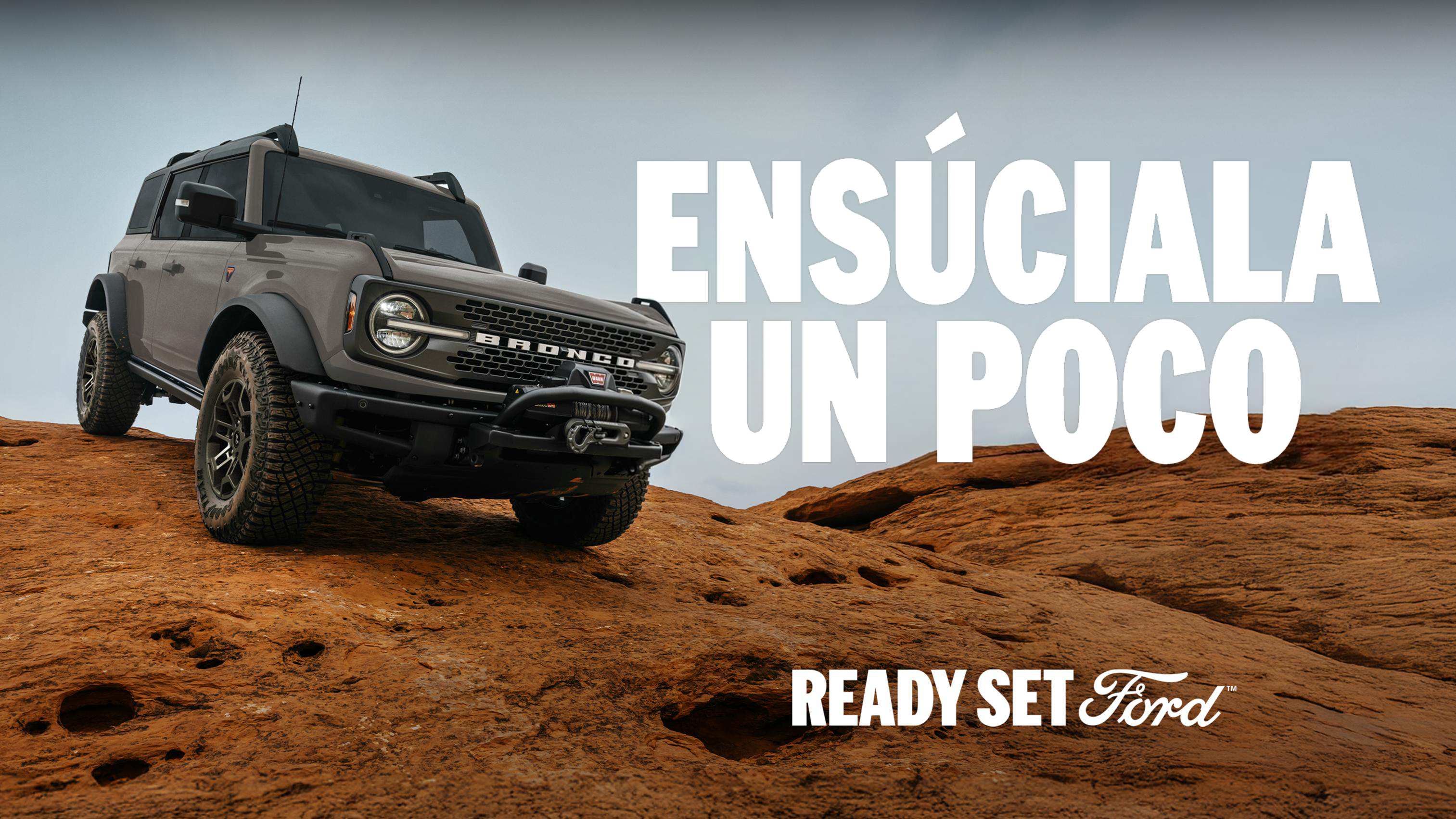 Camioneta Ford Bronco todoterreno sobre rocas con el texto 'Ensúciala un poco'.