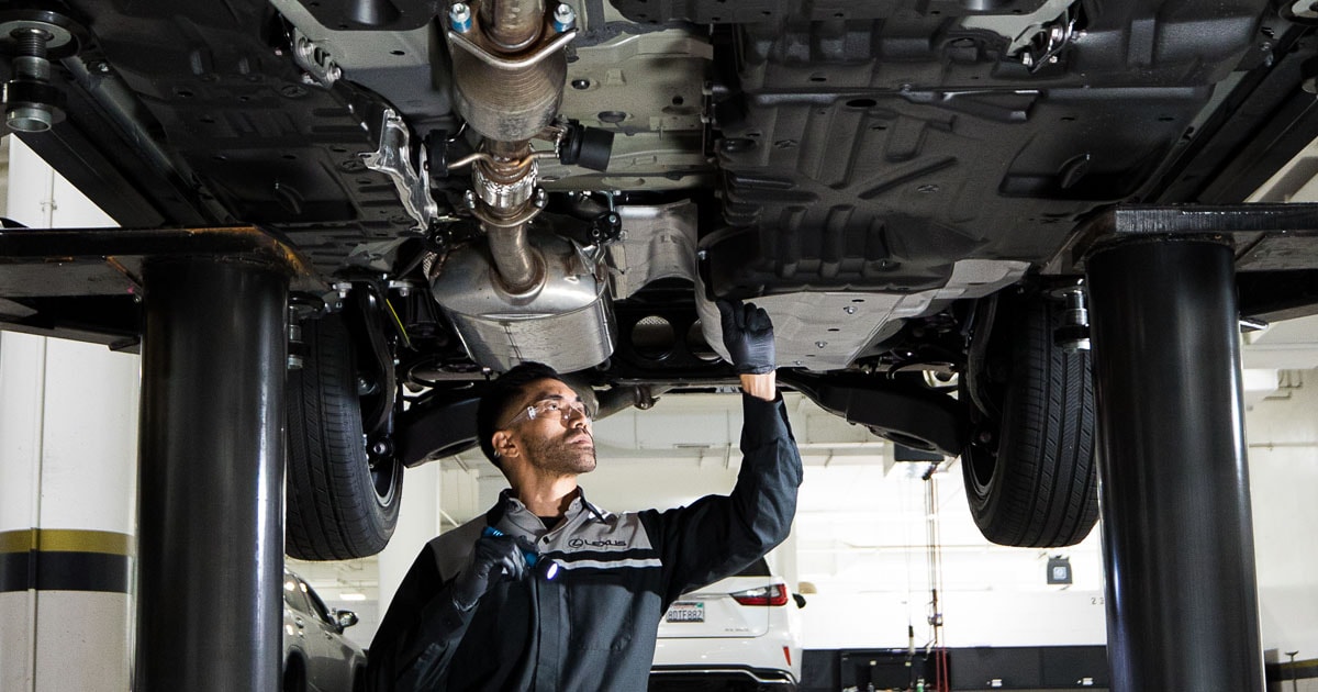 A Lexus service technician performing maintenance under a vehicle in the service center