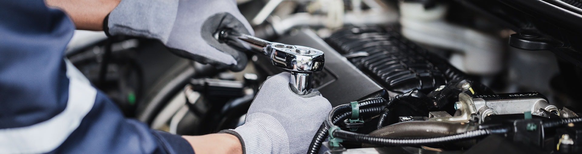 Close-up of a service technician's hands holding tools and working on a vehicle's engine.