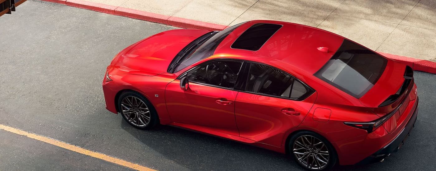 A red 2024 Lexus IS is shown parked on the side of a street from a side view.
