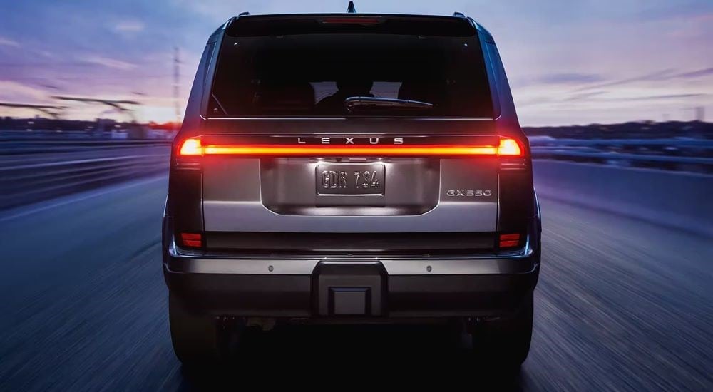 A grey 2024 Lexus GX 550 is shown from the rear driving on at dusk.