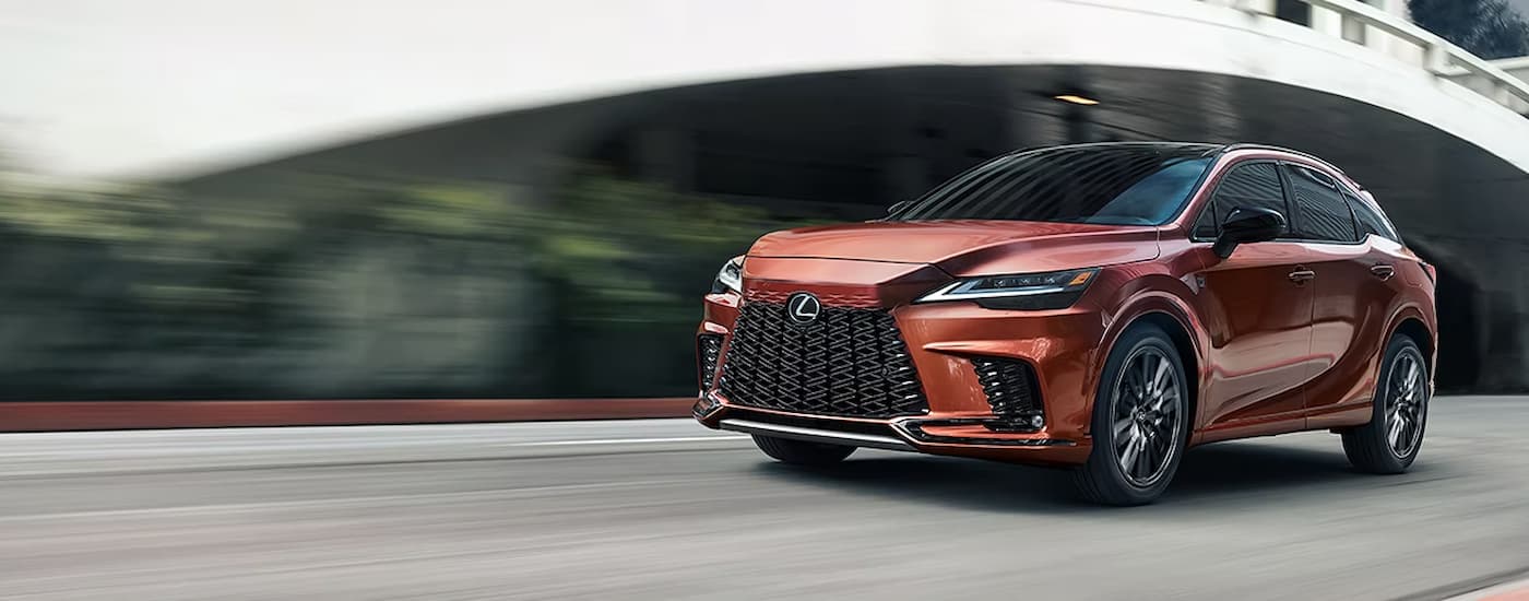 A brown 2023 Lexus RX 500h is shown driving next to a bridge. id=