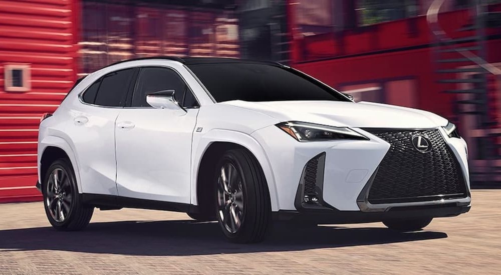 A white 2024 Lexus UXh is shown driving near a red building after visiting a Lexus dealer near White Plains.