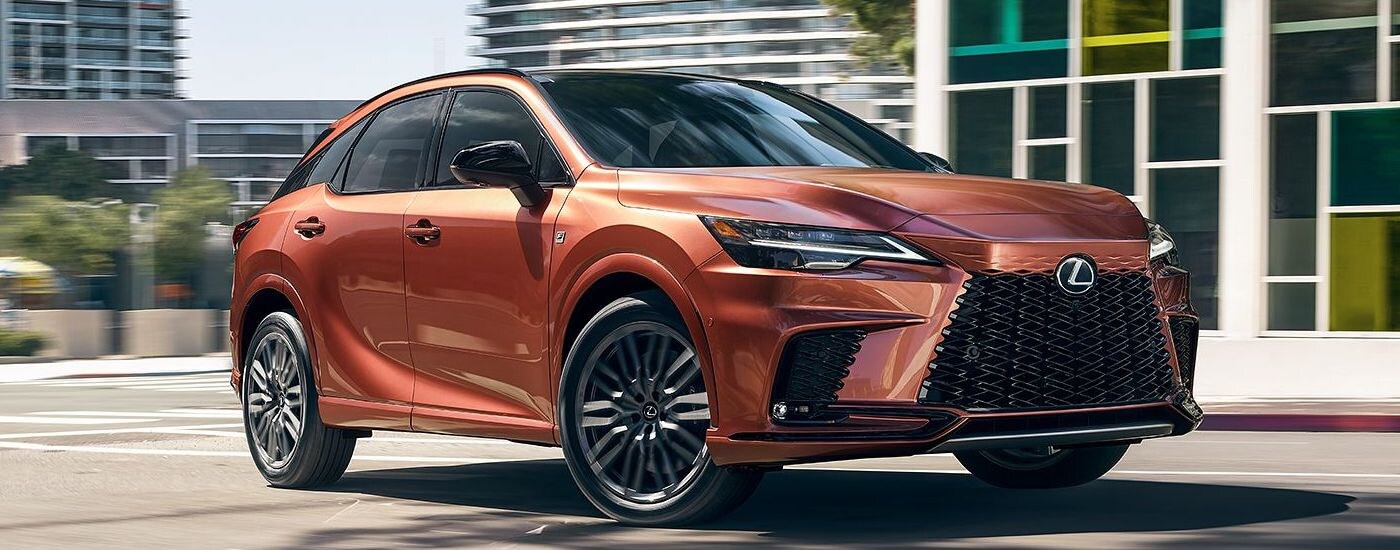 A copper colored 2024 Lexus RX F Sport driving in the city.