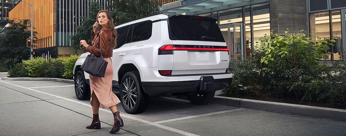 A woman is walking past a white 2024 Lexus GX 550 Luxury parked on the side of a street.