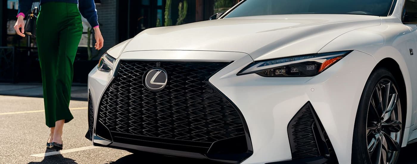 A woman in a green dress is shown walking towards a white 2024 Lexus IS for sale.