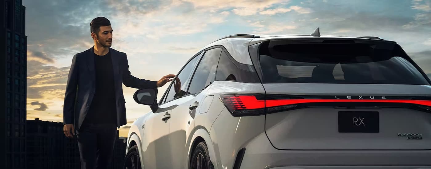 A man is shown walking next to a white 2023 Lexus RX with a blue sky view.