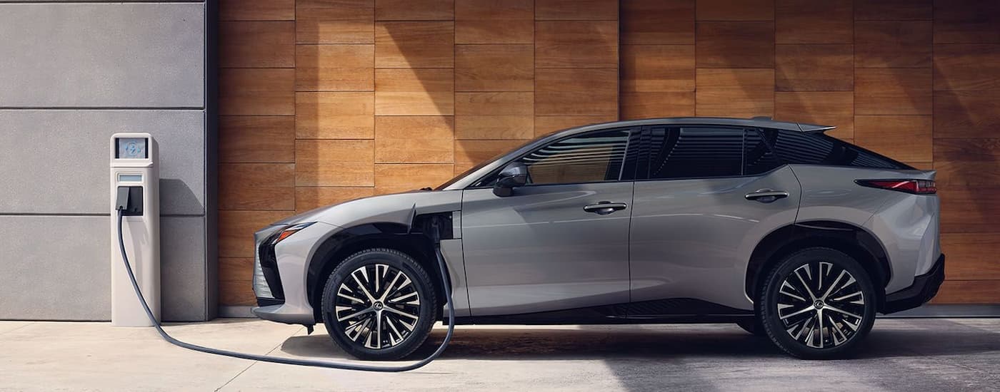 A grey 2023 Lexus RZ EV is shown from the side plugged into a charging station.