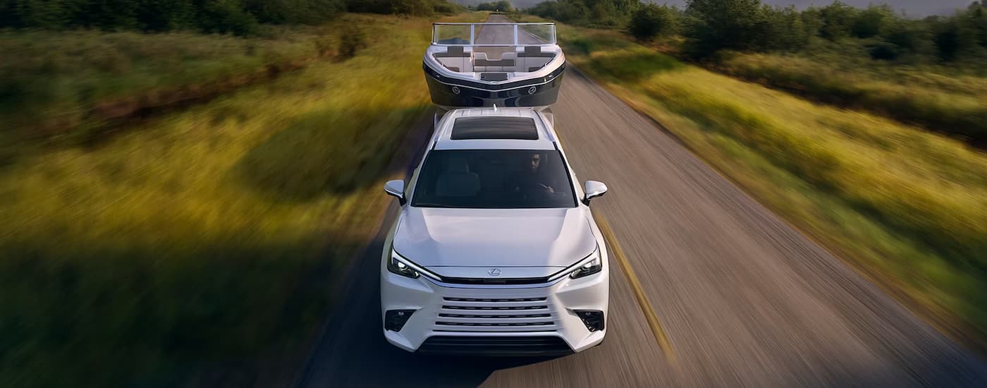 White 2026 Lexus TX towing a boat on a grass-lined road