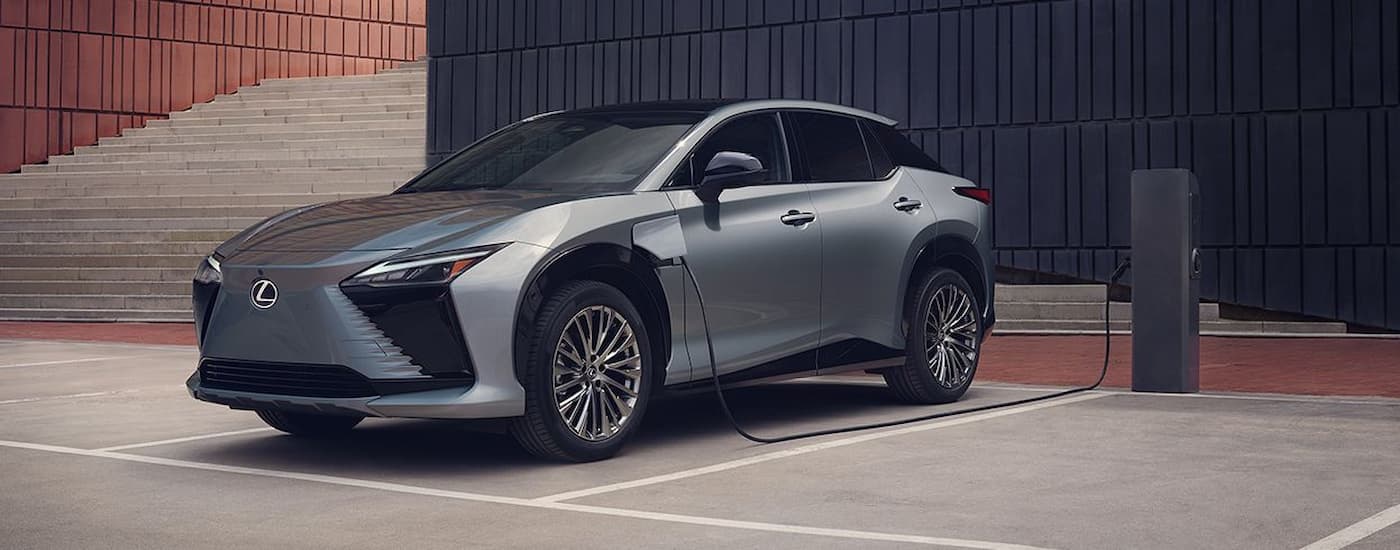 A silver 2023 Lexus RZ EV is shown parked a charging station in a parking lot.