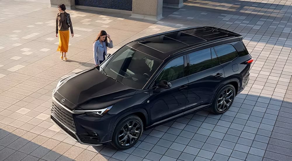 A black 2024 Lexus TX for sale is shown parked as two people walk towards it.