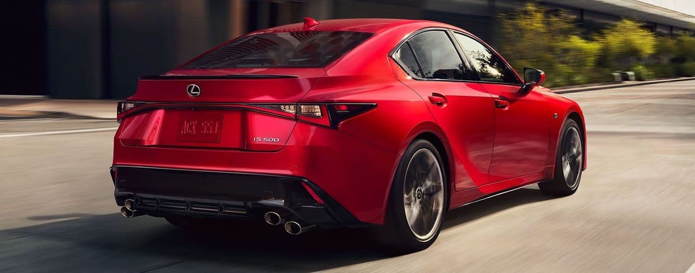 A red 2024 Lexus IS is shown from a rear angle driving on a city street.