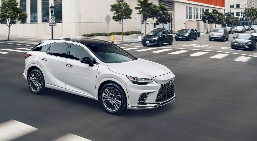  A white 2023 Lexus RX is shown driving on a city street after visiting a used Lexus dealership.
