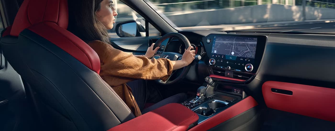 A woman is driving a 2025 Lexus NX with a black and red leather interior.