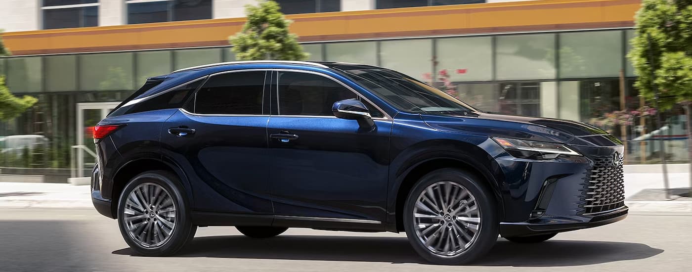 A blue 2024 Lexus RX for sale near Flushing is driving on a city street.