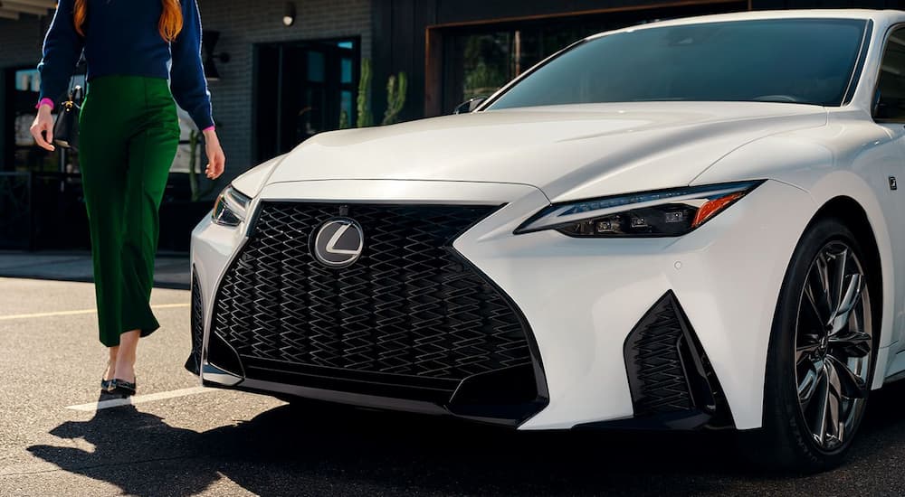 A woman is walking by a white 2024 Lexus IS parked in a lot.