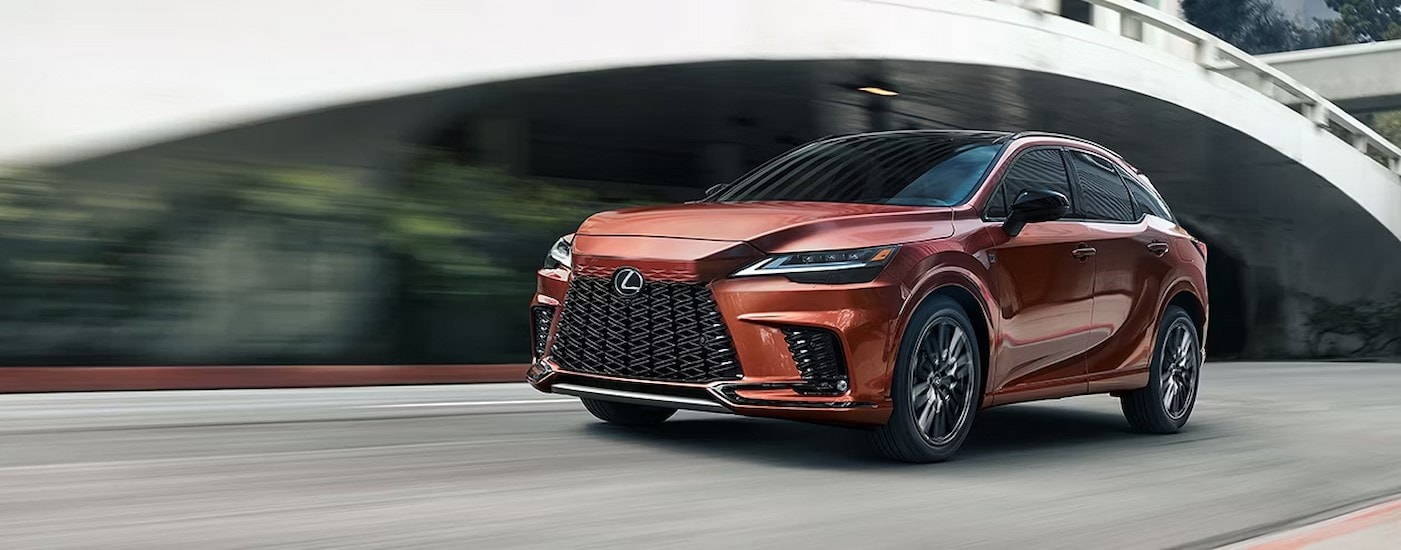 An orange 2024 Lexus RX F SPORT is shown driving near a bridge.