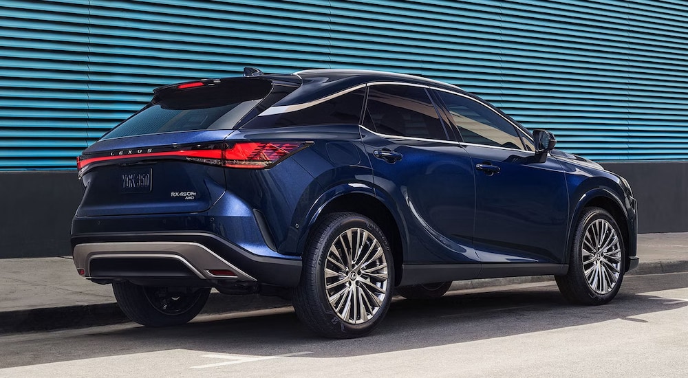 Rear view of a blue 2024 Lexus RX Hybrid parked in front of a blue wall.