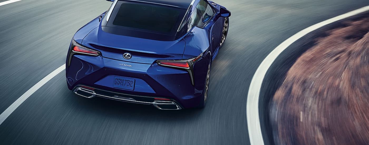 A blue 2024 Lexus LC Hybrid is shown from the rear driving on a winding road.