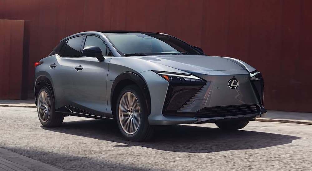 One of many popular Lexus EVs, a silver 2023 Lexus RZ, is shown parked near a red wall.  