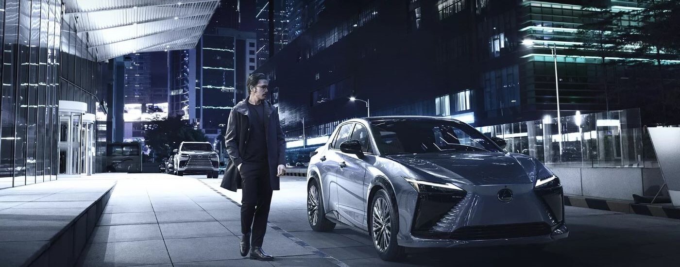 A silver 2023 Lexus RZ is shown a city street at night.
