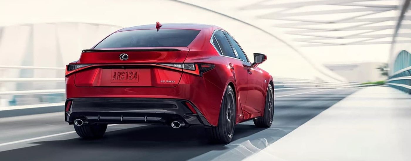 A red 2023 Lexus IS 350 is shown from the rear driving over a bridge.
