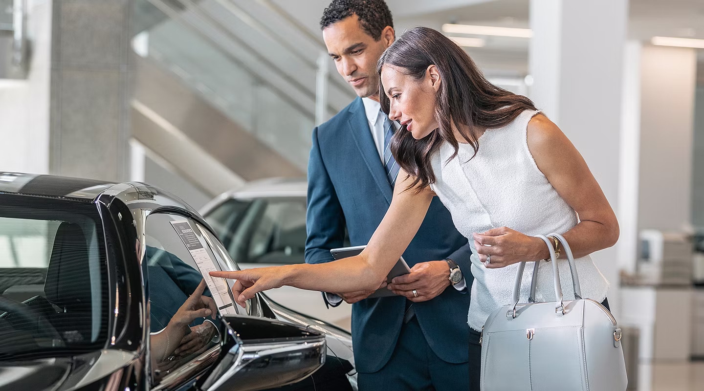  a woman and man looking at the sticker on the window of a lexus vehicle