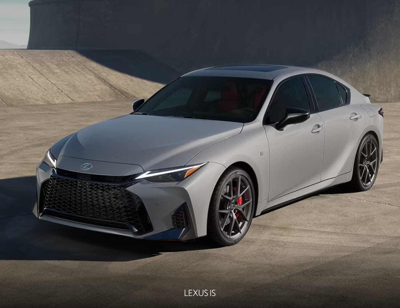 Front three-quarter view of a silver Lexus IS parked against a sleek concrete backdrop.