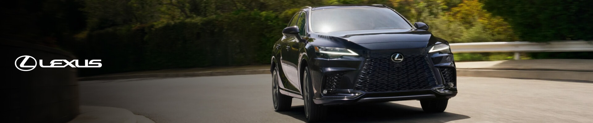 A front view action shot of a black 2026 Lexus RX cornering around a tree-lined switchback.