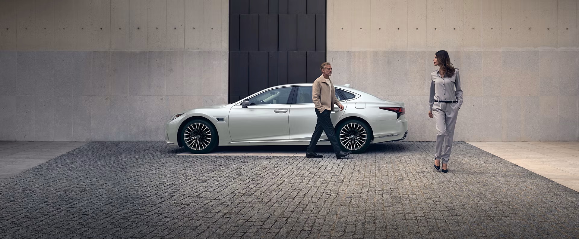 Couple in front of a 2025 Lexus LS Hybrid parked on a cobblestone street
