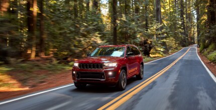 Jeep Grand Cherokee L red Jeep Grand Cherokee L driving in a forest