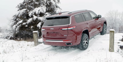 a red Jeep Grand Cherokee L driving up a hill in the snow