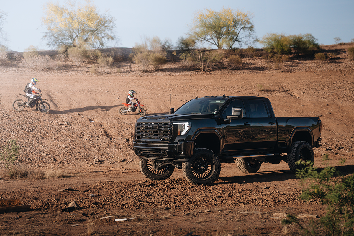  A father and son riding dirt bikes with a customized black GMC Sierra 1500 in the foreground