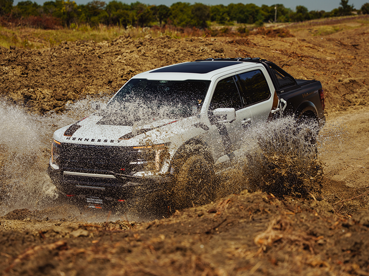  A Hennessey Ford F-150 Raptor driving through a puddle in a muddy field