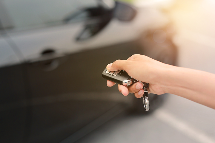  A person holding a vehicle key fob with a vehicle in the background