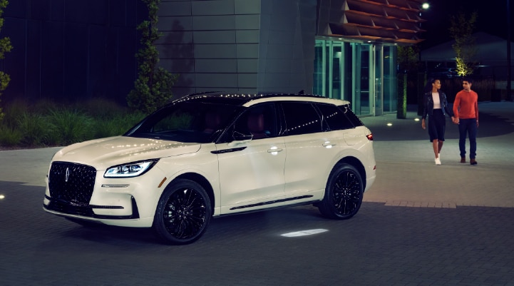A couple approaches a 2026 Lincoln Corsair® Reserve model as the Lincoln Embrace illumination guides the way