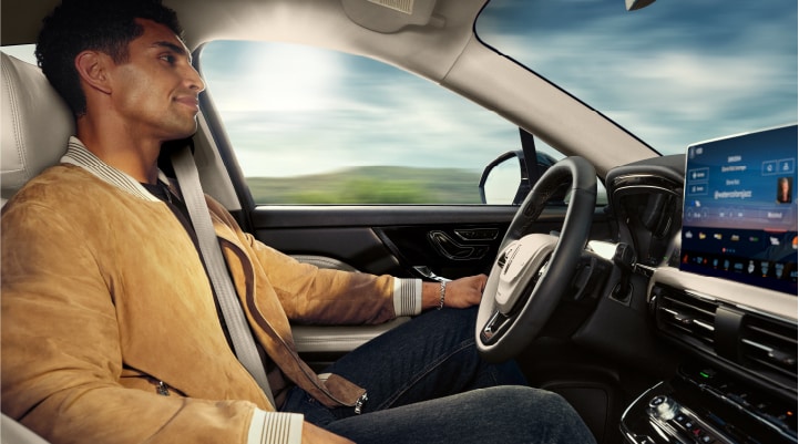 A person is shown using Lincoln BlueCruise hands-free highway driving technology on a divided highway in a hands-free Blue Zone.