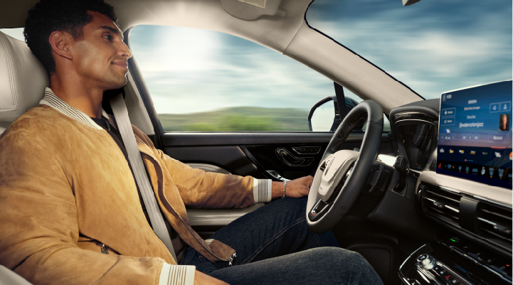 A person is shown using Lincoln BlueCruise hands-free highway driving technology on a divided highway called a Hands-Free Blue Zone.