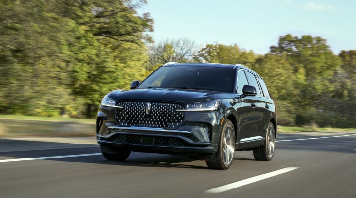 A 2025 Lincoln Black Label AviatorĀ® SUV is being driven down a road lined with trees.